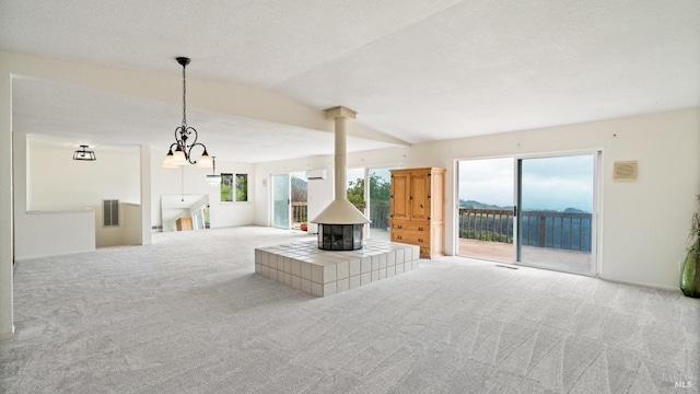 unfurnished living room with carpet, lofted ceiling, an inviting chandelier, visible vents, and a wood stove