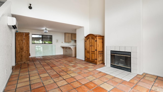 unfurnished living room featuring a tiled fireplace, a high ceiling, and a wall unit AC