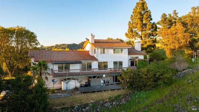 back of property featuring a chimney, a tile roof, a deck, and stucco siding