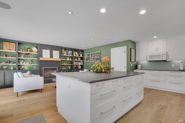 kitchen with light wood-style floors, a glass covered fireplace, white microwave, and white cabinetry