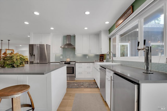 kitchen with wall chimney exhaust hood, appliances with stainless steel finishes, a sink, and plenty of natural light