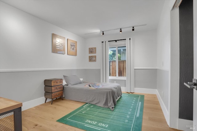 bedroom with rail lighting, baseboards, and wood finished floors