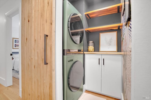 laundry area featuring cabinet space, stacked washer / dryer, and light wood finished floors