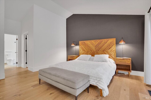 bedroom featuring baseboards, an accent wall, light wood-type flooring, and high vaulted ceiling