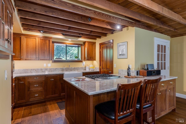 kitchen with stainless steel gas stovetop, a kitchen breakfast bar, a sink, light stone countertops, and brown cabinetry