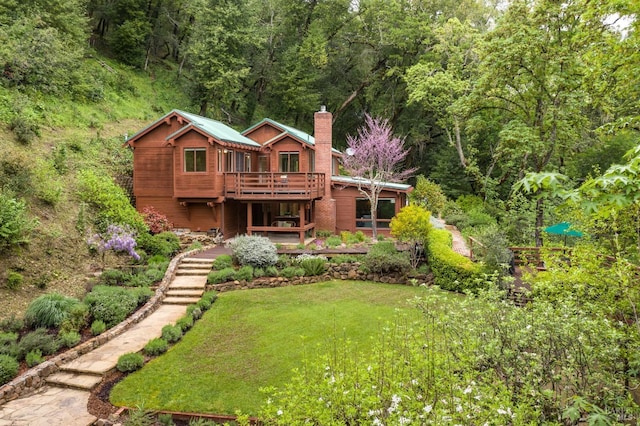 rear view of property featuring a chimney, a forest view, a yard, and a deck