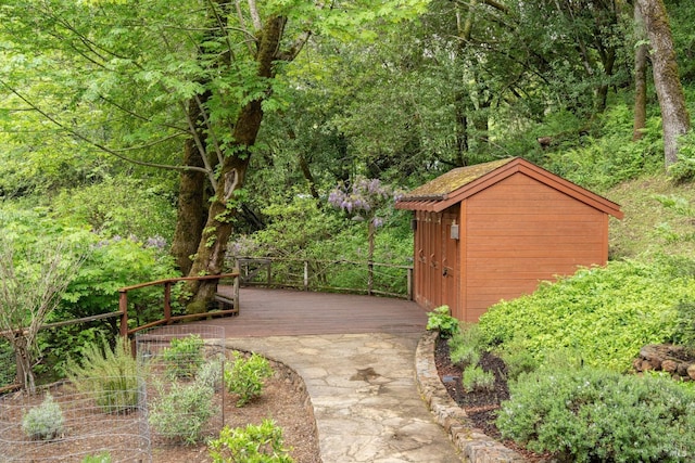 view of community with an outdoor structure, a deck, a wooded view, and a storage shed