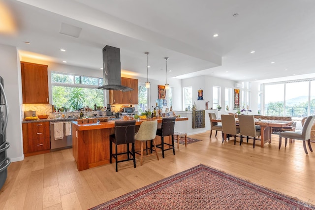 kitchen featuring stainless steel dishwasher, brown cabinetry, light wood-style flooring, and island range hood