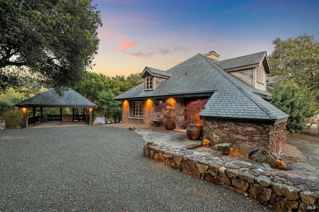 back of property at dusk with a gazebo, stone siding, and a chimney