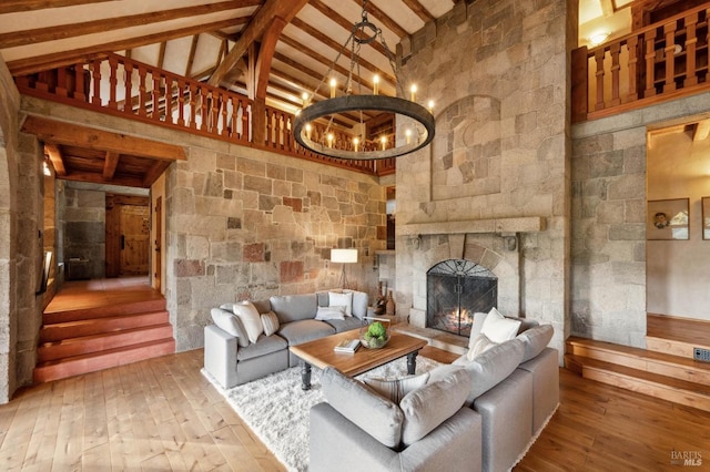 living room with high vaulted ceiling, hardwood / wood-style flooring, an inviting chandelier, a fireplace, and beam ceiling