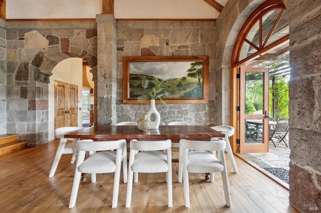 dining room with wood-type flooring, arched walkways, and lofted ceiling