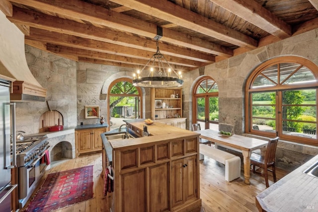 kitchen featuring a kitchen island with sink, light wood-style flooring, beam ceiling, double oven range, and wood ceiling