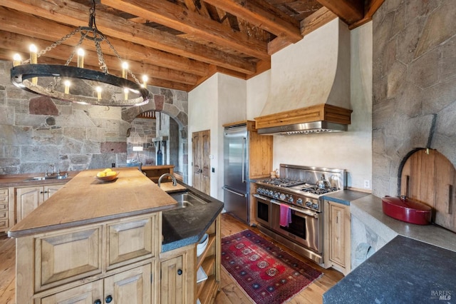 kitchen featuring a kitchen island with sink, a sink, custom exhaust hood, high end appliances, and beamed ceiling