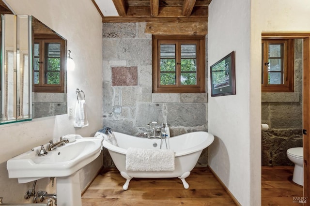 full bathroom with toilet, a soaking tub, wood finished floors, and beamed ceiling