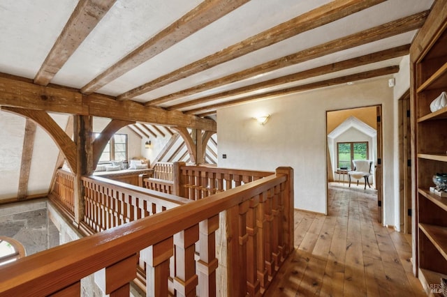 corridor with hardwood / wood-style flooring, beam ceiling, and an upstairs landing