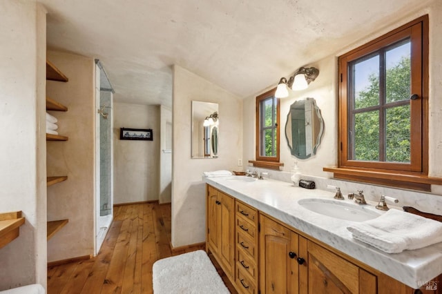 bathroom with vaulted ceiling, a sink, hardwood / wood-style flooring, walk in shower, and double vanity