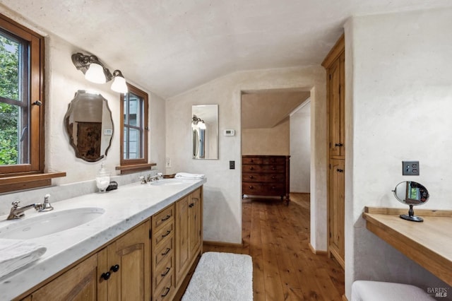 full bathroom featuring wood-type flooring, vaulted ceiling, a sink, and double vanity