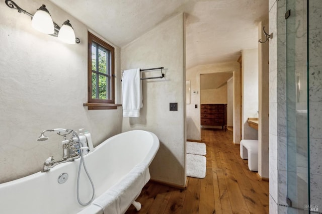 full bath with lofted ceiling, a freestanding bath, and wood-type flooring