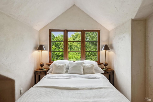 bedroom with lofted ceiling and a textured wall