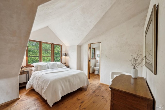 bedroom with hardwood / wood-style floors, ensuite bathroom, and lofted ceiling