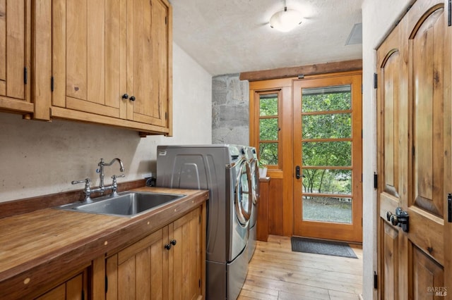 clothes washing area with cabinet space, washer and clothes dryer, light wood finished floors, and a sink