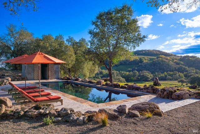 pool with a storage structure, an outdoor structure, a mountain view, and a patio
