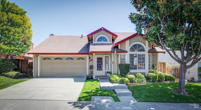 traditional-style house with fence, a shingled roof, a front lawn, concrete driveway, and an attached garage