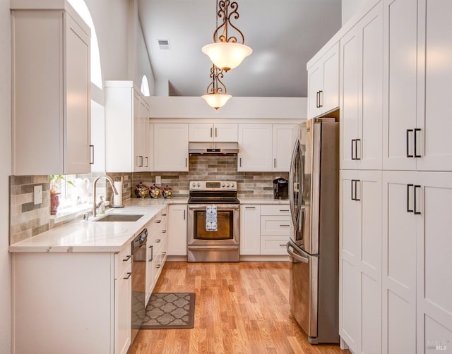 kitchen with a sink, stainless steel appliances, light wood finished floors, white cabinets, and light stone countertops