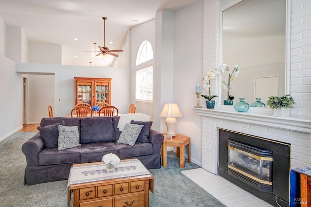 living room with high vaulted ceiling, a tiled fireplace, a ceiling fan, and light colored carpet