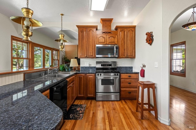 kitchen featuring light wood finished floors, stainless steel appliances, arched walkways, a sink, and brown cabinets