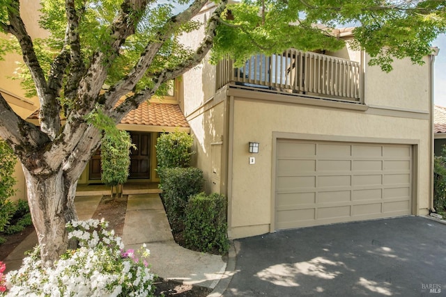view of front of home featuring aphalt driveway, a tiled roof, a balcony, stucco siding, and an attached garage