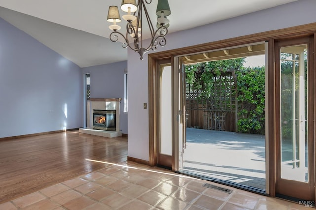 entryway with vaulted ceiling, a glass covered fireplace, baseboards, a notable chandelier, and visible vents
