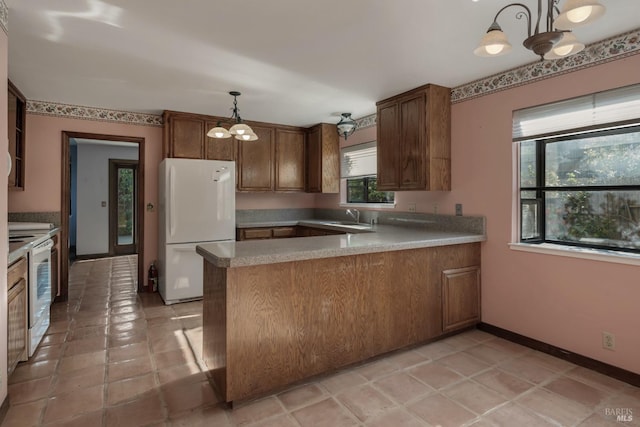 kitchen with a peninsula, white appliances, a sink, and a notable chandelier