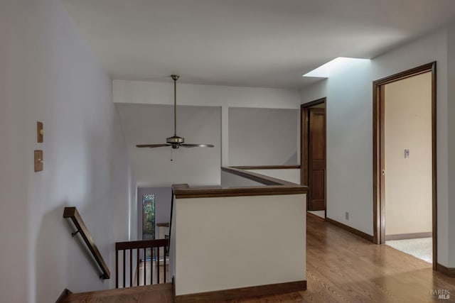 hallway featuring baseboards, wood finished floors, and an upstairs landing