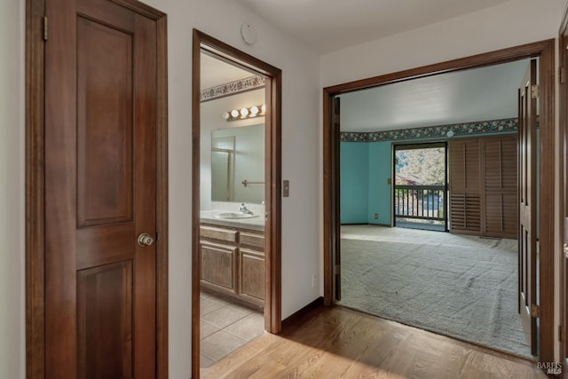 hallway with light wood finished floors, light carpet, baseboards, and a sink