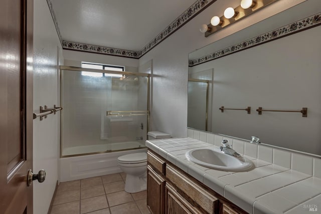 full bathroom featuring combined bath / shower with glass door, tile patterned flooring, vanity, and toilet