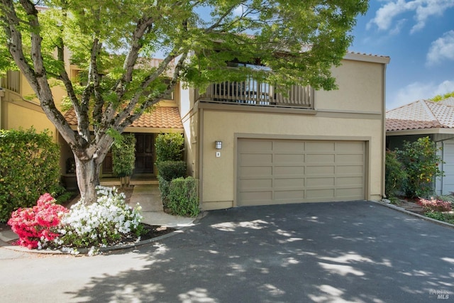 mediterranean / spanish home featuring aphalt driveway, a tiled roof, a balcony, and stucco siding
