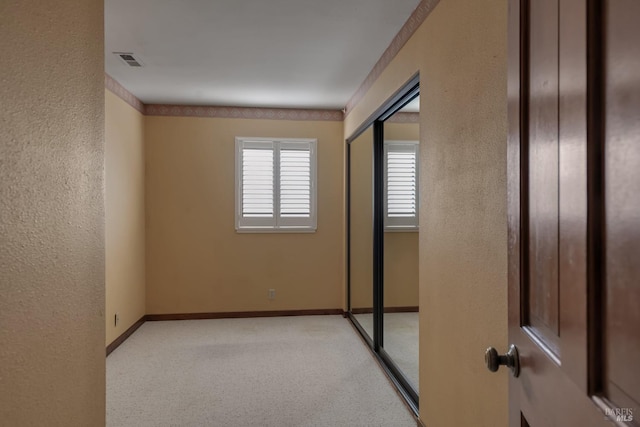 empty room with carpet floors, a textured wall, visible vents, and baseboards