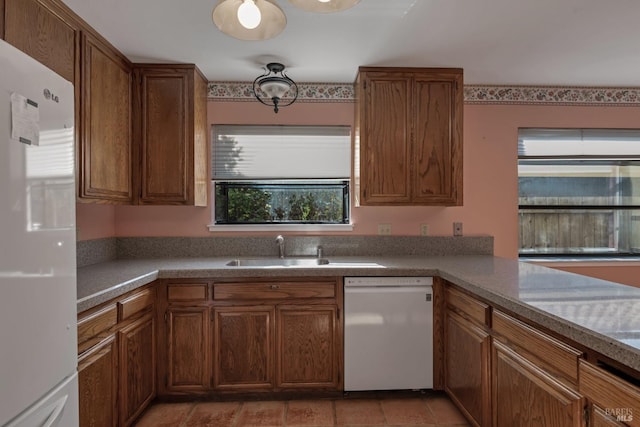 kitchen with brown cabinetry, a sink, and white appliances