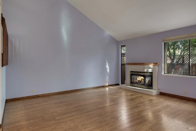 unfurnished living room featuring lofted ceiling, a glass covered fireplace, wood finished floors, and baseboards