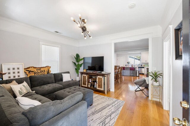 living area with light wood finished floors, visible vents, an inviting chandelier, and ornamental molding