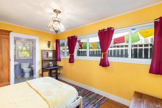 bedroom featuring crown molding, baseboards, ensuite bathroom, and wood walls