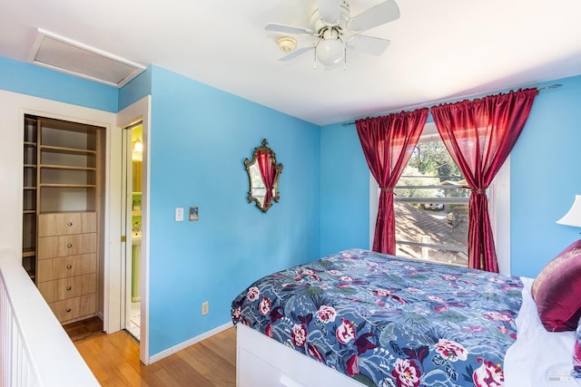 bedroom featuring attic access, baseboards, wood finished floors, and ceiling fan