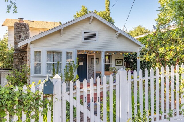 bungalow-style home with a chimney, fence, and covered porch