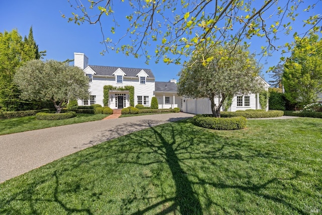 view of front facade featuring driveway, a chimney, and a front yard