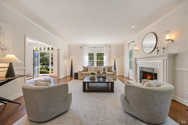 living room with wood finished floors, a brick fireplace, baseboards, and ornamental molding