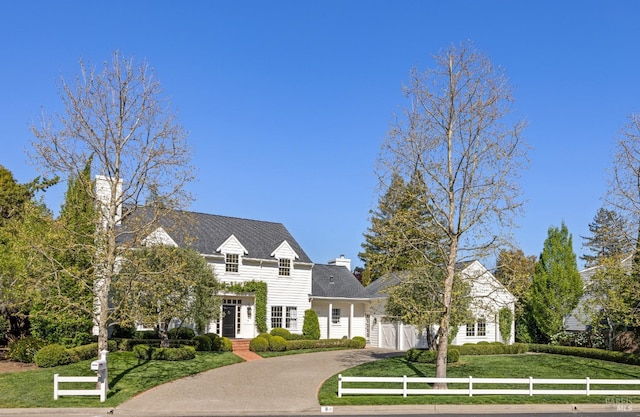 french country inspired facade with fence, driveway, a front lawn, and a chimney