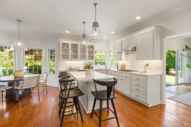 kitchen with tasteful backsplash, a sink, glass insert cabinets, light countertops, and dark wood-style floors