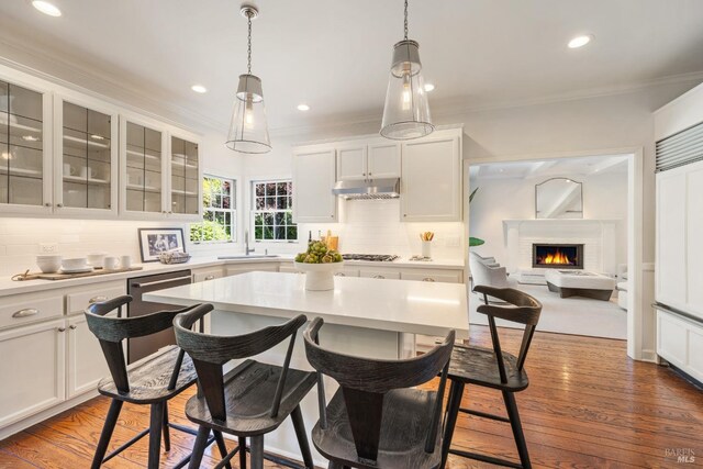 kitchen featuring crown molding, a sink, decorative backsplash, a kitchen bar, and under cabinet range hood