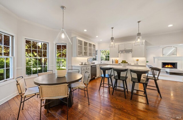 dining room featuring crown molding, a warm lit fireplace, recessed lighting, and dark wood-style flooring